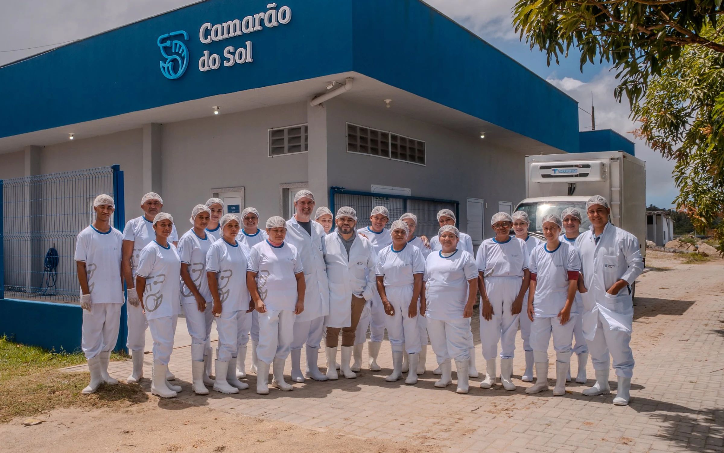A sede da indústria Camarão do Sol, com a equipe de uniforme na frente do prédio